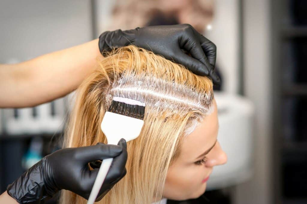 woman receives a balayage treatment with stylist applying color to hair roots using a brush