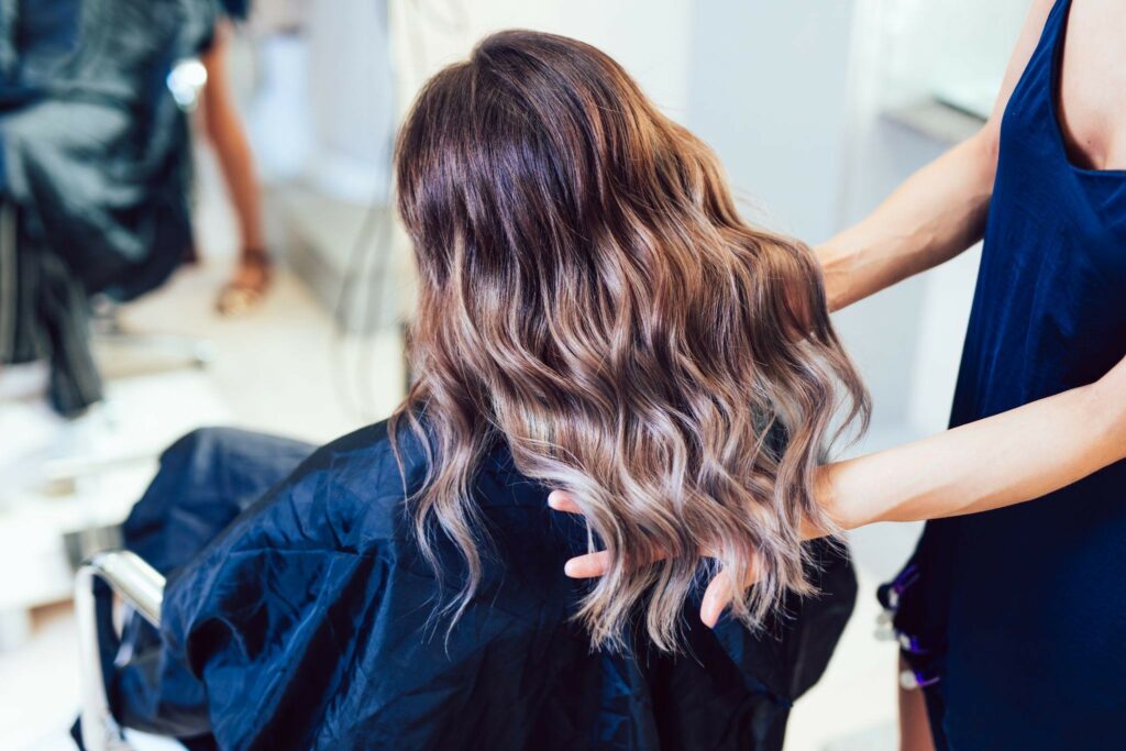 a woman sits in a salon chair while a stylist examines the finished coloring treatment